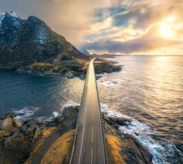 Canvas Print - Aerial view of bridge, sea with waves and mountains at sunset in Lofoten Islands, Norway. Landscape with beautiful road, water, rocks, blue sky with clouds and golden sunlight. Top view from drone