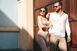 Beautiful fashion woman and her handsome elegant boyfriend in white shirt. Sexy smiling model in summer clothes. Fashionable smiling couple posing in street near wall. Brutal man and female outdoors