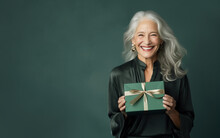 Beautiful mature woman 50, 60, 70 years old on a green background holding a large gift box, holiday surprise, compliment bonus for birthday anniversary