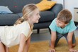 © Studio Marmellata - Cheerful little girl and boy in casual clothes practicing Chakravakasana yoga pose on carpet in living room at home
