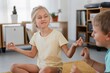 © Studio Marmellata - Cheerful girl in casual clothes practicing Lotus Pose with brother on carpet in living room at home