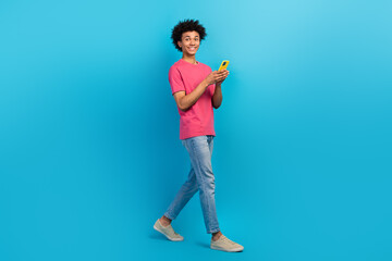 Poster - Full size photo of handsome young male walking hold telephone share post wear trendy pink outfit isolated on blue color background