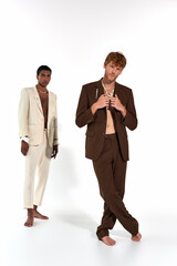 handsome interracial friends posing barefoot in elegant suits with accessories, looking at camera