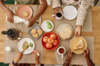 © AnnaStills - Hands of family eating breakfast at kitchen table, view from above