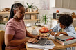Black woman working on laptop at home when her son doing homework