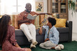 © AnnaStills - Boy and girl sitting on floor and listening to father reading book on Black History