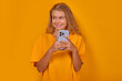 © antianti - Young laughing Caucasian woman with phone in hands chatting in mobile messenger and exchanging messages with friends from social networks dressed in casual style stands on yellow background