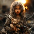 A little girl in an empty city destroyed by war, refugees without a home and parents, stop the war and aggression. In hands with a plush toy and a weapon for self-defense