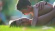 Affectionate moment of little son kissing mother in cheek while laid on grass during summer day vacations. Family lifestyle depicting love and care, skin-to-skin