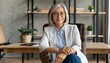 © Marko - Middle aged female psychotherapist, counselor sitting in chair alone in office looking at camera. Sophisticated elegant mature 50s woman of mid age with blond hair posing indoors