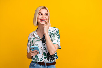 Wall Mural - Photo portrait of lovely young lady device bite interested nail dressed stylish leaves print garment isolated on yellow color background