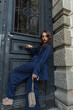 © alones - Beautiful fashionable street woman model with hairstyle in a fashion blue suit with a bag and trendy shoes stands and poses near a vintage door in the city