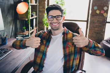 Photo of happy web designer sitting chair hands fingers demonstrate thumb up approval workstation office indoors