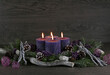 Adventsdekoration: Adventskranz mit vier lila brennenden Kerzen für den vierten Advent mit Tannenzweigen und Weihnachtsdeko vor einer Holzwand mit Platz für Text.