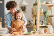 © Mediaphotos - Happy young mom teaching her son to cut vegetables for salad while they cooking together in kitchen
