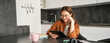 © Mix and Match Studio - Portrait of young woman working from home, connecting to lesson on digital tablet, reading in glasses, studying remotely in her kitchen, distance learning and education concept