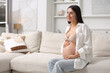 © New Africa - Beautiful pregnant woman sitting on sofa at home