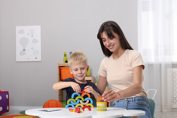 Sticker - Motor skills development. Happy mother helping her son to play with colorful wooden arcs at white table in room