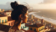 Photo in landscape ratio 9:16 of a Latin girl's upper body, shot from behind. She gazes out over a coastal city with terracotta rooftops and the sea in the distance. Her hair is tied up, revealing int