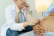 © DG PhotoStock - Asian male doctor visit to African - American pregnant woman patient home to talk and check for pregnancy health. On site - home medical service concept.