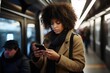 African American lady holds phone in hand scrolling through messages. Woman in metro remains absorbed in glow of screen of smartphone disconnected from noise engaging with digital content