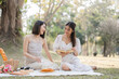 © wichayada - Two beautiful LGBT young women in casual clothes and summer hats Carefree woman having a picnic outside Positive model sitting on the grass eat fruit and cheese Take a selfie. LGBT concept