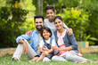 © WESTOCK - Happy indian couple with kids embracing by looking at camera while sitting at park - concept of relationship, family time and togetherness