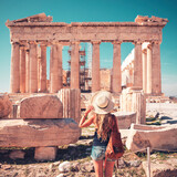 Travel destination in Athens- Young woman tourist with hat and bag looking at old ruin temple, Parthenon in Acropolis, Greece