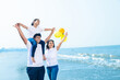 Happy young indian family of three wearing white t-shirt and blue jeans walking at beach, .Father carrying his daughter on shoulders, enjoying summer vacations. Travel and holidays.