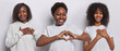 Horizontal shot of cheerful overweight African woman shows heart gesture stand between two other women who make gratitude gesture say thank you dressed casually isolated over white background