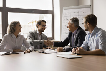 Canvas Print - Happy successful businessmen enjoying teamwork, partnership, team success, shaking hands over meeting table, smiling, laughing, reaching agreement, giving greeting handshakes