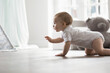 © fizkes - Side view cute pretty girl or baby boy in bodysuit crawling on warm floor in cozy living room. Little toddler exploring surroundings, creeping alone in modern playroom. Development, growth, babyhood