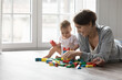 Attractive loving mother play with infant toddler on warm floor, young mum help build tower from colorful wooden cubes, enjoy learning activity with cute baby at home. Development, motherhood, games