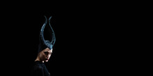 Beautiful Woman With Devil Witch Horns In Sorceress Costume. Woman In Halloween Costume Posing Against Black Background.