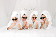 © wedmoments.stock - Young, beautiful women in bathrobes and glasses enjoying bachelorette party at spa or hotel and eating donuts, happy multiracial girlfriends celebrating bachelorette party
