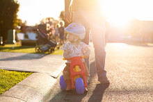 Young Aussie Kid Playing On Trike On Street At Sunset With Parent Watching