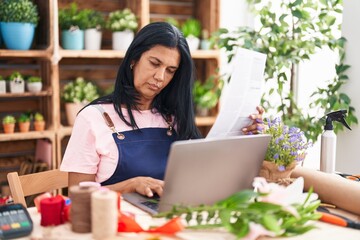 Wall Mural - Middle age hispanic woman florist using laptop reading document at florist