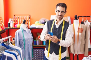 Canvas Print - Young hispanic man tailor smiling confident using smartphone at atelier