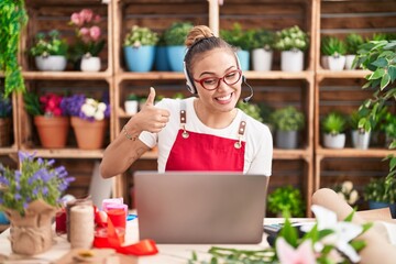 Sticker - Young hispanic woman working at florist shop doing video call smiling happy and positive, thumb up doing excellent and approval sign