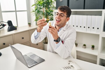 Canvas Print - Young hispanic man optician smiling confident holding medication bottle at clinic