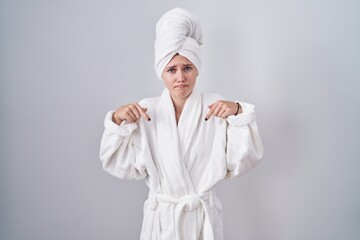 Canvas Print - Blonde caucasian woman wearing bathrobe pointing down looking sad and upset, indicating direction with fingers, unhappy and depressed.