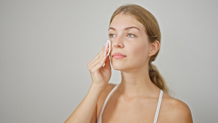 Wall Mural - Young blonde woman cleaning face with cotton pad over isolated white background