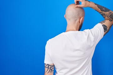 Poster - Hispanic man with tattoos standing over blue background backwards thinking about doubt with hand on head