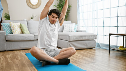 Sticker - Young latin man sitting on floor training yoga stretching back and arms at home