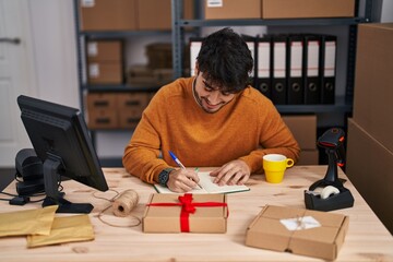 Poster - Young hispanic man ecommerce business worker writing on notebook drinking coffee at office