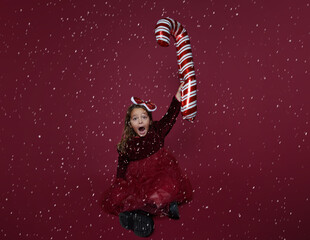 Christmas concept. Adorable little girl holding a sugar cane on isolated red background. funny capture