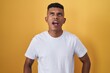 © Krakenimages.com - Young hispanic man standing over yellow background angry and mad screaming frustrated and furious, shouting with anger. rage and aggressive concept.