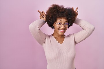 Sticker - Young african american woman standing over pink background posing funny and crazy with fingers on head as bunny ears, smiling cheerful