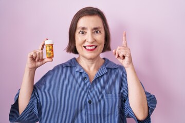 Wall Mural - Middle age hispanic woman holding pills surprised with an idea or question pointing finger with happy face, number one