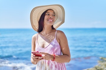 Canvas Print - Young beautiful hispanic woman tourist smiling confident using smartphone at seaside